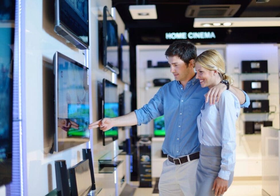 A man and woman looking at some televisions