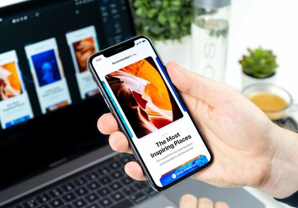 A person holding an iphone in front of a laptop.